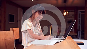 Young Asian Girl Home Schooling Working At Table Using Laptop photo