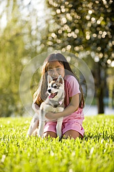 Young Asian girl hugging puppy sitting on grass