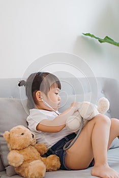 A young Asian girl playing doctor with her brown teddy bear