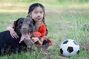 A young Asian girl playing football with her big black dog outside the grass ground in the yard in the evening