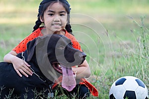 A young Asian girl playing football with her big black dog outside the grass ground in the yard in the evening