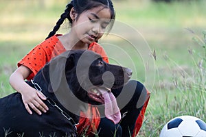 A young Asian girl playing football with her big black dog outside the grass ground in the yard in the evening