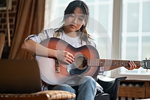 Young asian girl playing the guitar at home