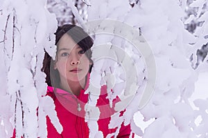 Young Asian girl standing behind snow covered branches