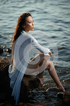 Young asian girl in swimsuit and long shirt relax on seashore at sunset