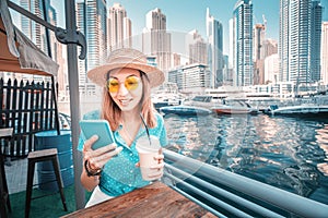 Young Asian girl texting on her phone and reading news on social networks in the beautiful Marina port in Dubai