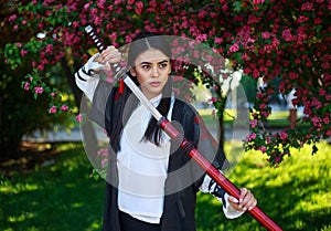 Young asian girl in traditional kimano in a blooming garden with samurai japanese sword katana in image of warrior woman