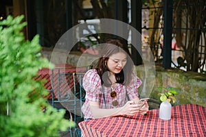 Young asian girl using smartphone waiting for her friend to come at restaurant.