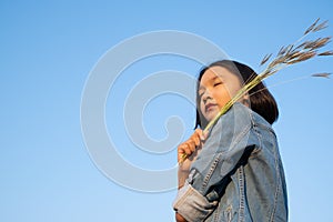 Young asian girl wear Jetket Jean hold grass flower .Blue sky background