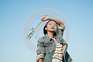 Young asian girl wear Jetket Jean hold grass flower .Blue sky background