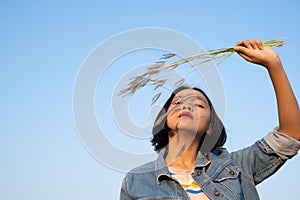 Young asian girl wear Jetket Jean hold grass flower .Blue sky background