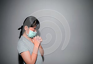 A young Asian girl wearing a mask to prevent PM2.5 and COVID-19 is at home, praying to God, worshiping on the day of the coronavir