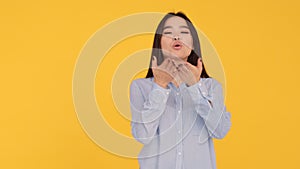 Young Asian girl on yellow background sends air kiss and smiles