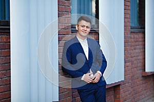 A young Asian guy in a blue suit stands against the wall and looks to the left of the viewer. Street photo