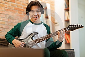 Young Asian Guy Practicing Guitar Chords Looking At Laptop Indoor