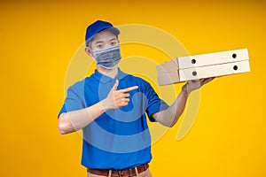 Young Asian handsome delivery man wearing mask pointing to pizza boxes