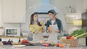 Young Asian happy active family couple dancing laughing together preparing food at home