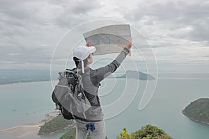 Young Asian hipster man with bag exploring map on viewpoint of mountain. Travel and adventure concept.