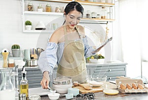 Young Asian housewife in kitchen using tablet for searching recipes online cooking the bakery dough homemade