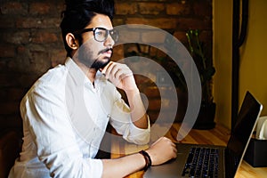 Young Asian Indian businessman using a laptop during office break at cafe, relaxing with a cup of coffee.