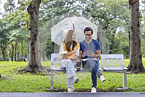 Young Asian and Indian couple enjoy having relaxing time in the rain together in the public park while sitting together on the
