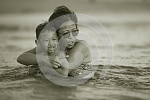 Young Asian Indonesian mother and little son enjoying summer holidays having a bath on the sea at tropical beach in family