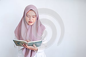 Young Asian Islam woman wearing headscarf is praying or read Quran - the holy book of Islam with smile and serious face.