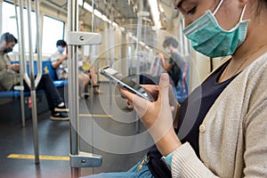Young Asian Japanese woman wearing face mask and using smart phone in BTS subway train Bangkok city, Thailand. Social distancing