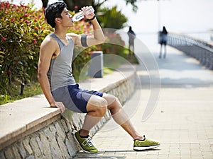 Young asian jogger resting and drinking water