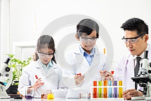 Young Asian kids wearing white scientist gown and do chemical test tube while study, learning in science classroom with teacher.