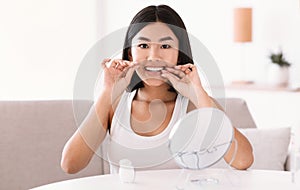 Young asian lady using dental floss looking in mirror