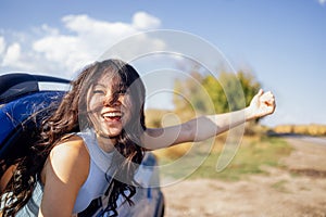 A young Asian leans out of the car window and laughs. A smiling Korean woman travels and has fun on the road photo