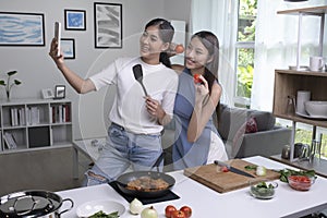 Young Asian lesbian couple looking happy while cooking and taking selfie. LGBT couple preparing meal salad in the kitchen at home