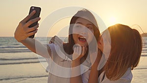 Young Asian lesbian couple using smartphone taking selfie near beach. Beautiful women lgbt couple happy relax enjoy love moment