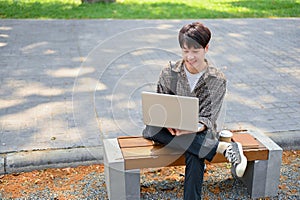 A young Asian male college student using his laptop computer on a bench in the campus park