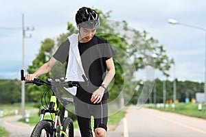 Young asian male cyclist with injured knee carry bicycle walk in park after an accident