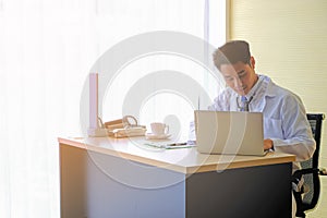 Young  Asian male doctor with stethoscope using a laptop in the hospital room