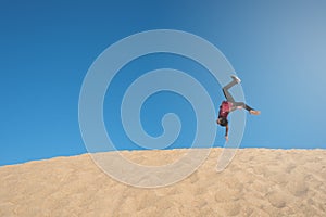 Young asian male make an acrobatic backflip moves on a sand dune