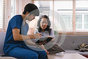 Young Asian male nurse, assisted living in-home carer, or doctor visiting an old senior citizen at home to talk about