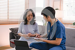 Young Asian male nurse, assisted living in-home carer, or doctor visiting an old senior citizen at home to talk about