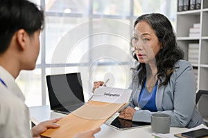 A young Asian male office employee giving a resignation letter to a female boss