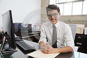 Young Asian male professional at desk smiling to camera
