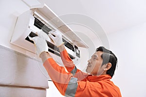 Young asian male technician repairing air conditioner