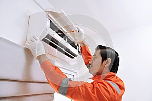 Young asian male technician repairing air conditioner with