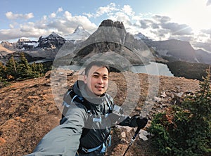 Young asian male traveler taking selfie portrait on the hill with mount assiniboine in national park