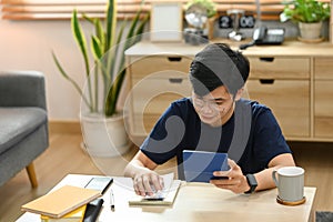 Young asian male using calculator for calculating money bank loan rent payments, managing expenses finances