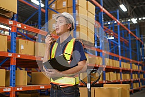Young asian male worker wearing helmet using talki walki in modern warehouse