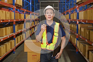 Young asian male worker wearing helmet using talki walki in modern warehouse