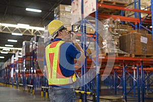 Young asian male worker wearing helmet using talki walki in modern warehouse