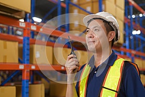 Young asian male worker wearing helmet using talki walki in modern warehouse